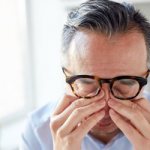 A man rubs his eyes because of pain in his eyes